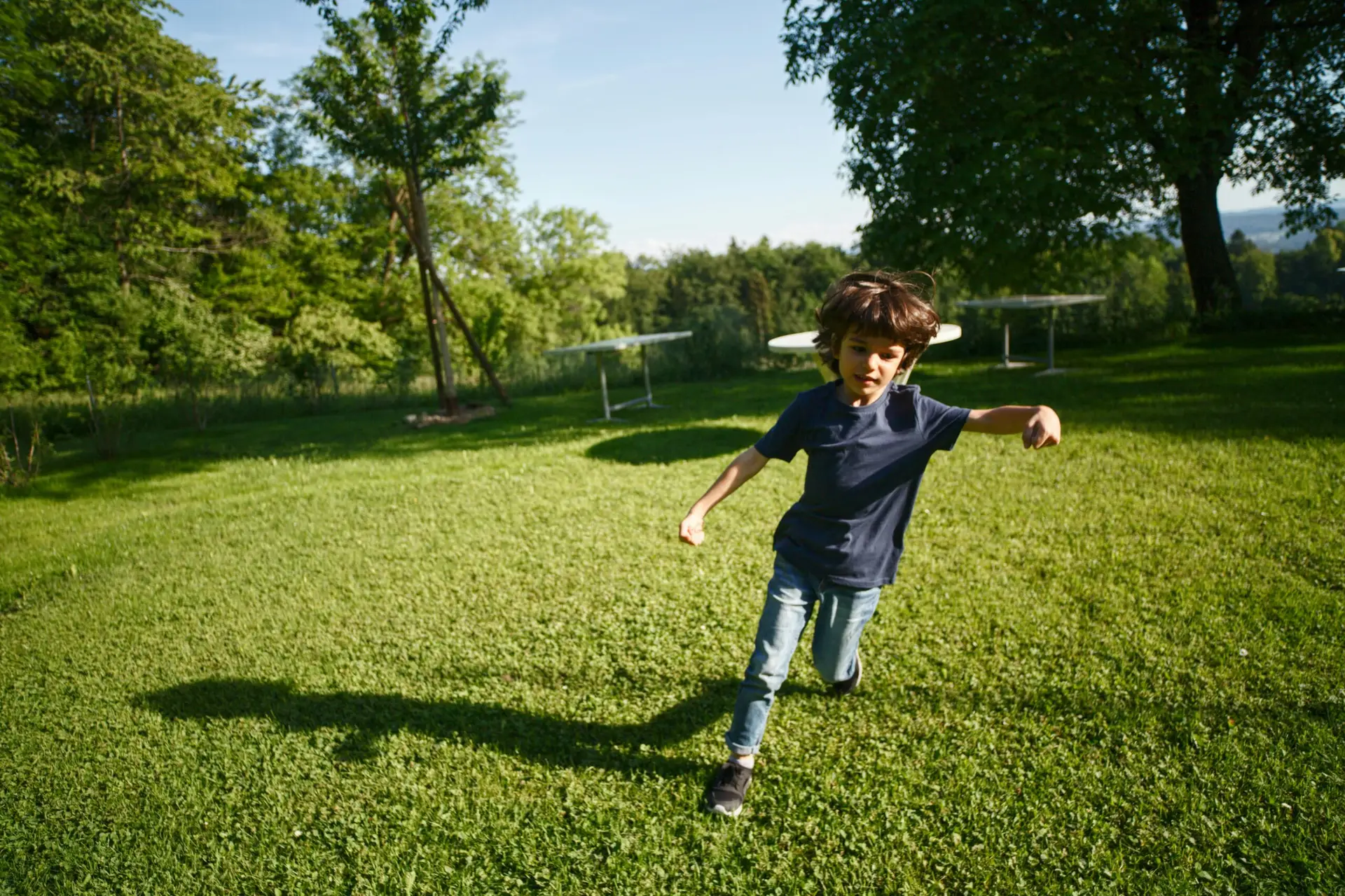 A joyful child running on a grassy field in a sunny park, enjoying nature and leisure time.
