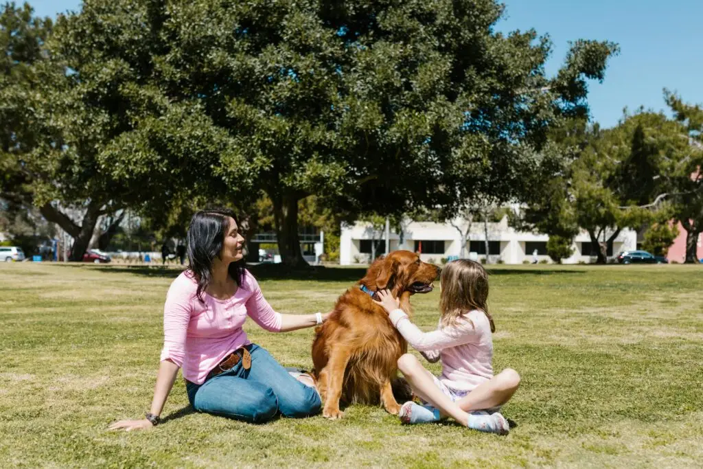 Mother and daughter enjoying time outdoors with their golden retriever on a sunny day.