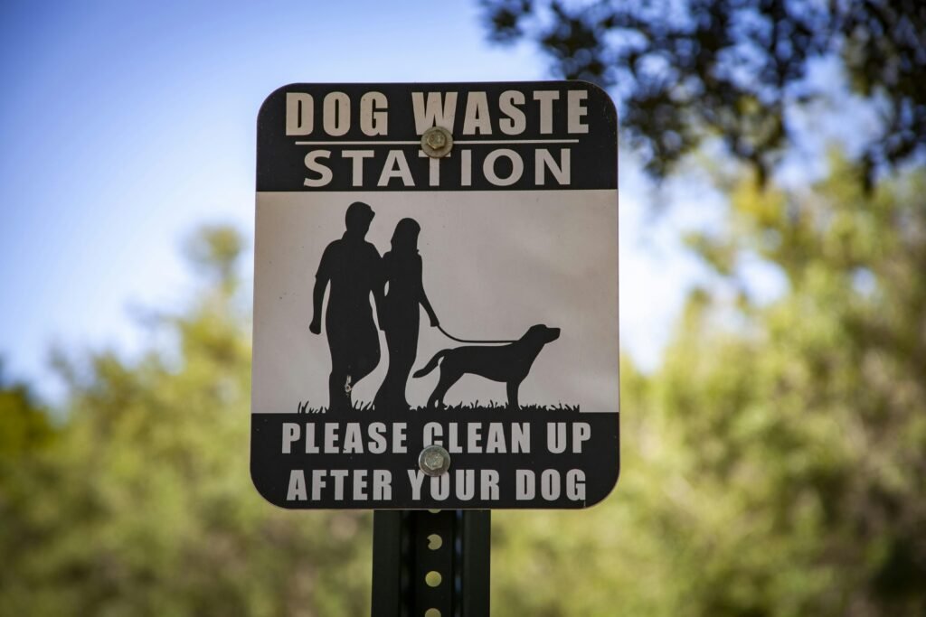 A dog waste station sign in a park reminding pet owners to clean up after their dogs.